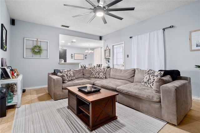 living room with ceiling fan with notable chandelier, light tile patterned floors, and a textured ceiling