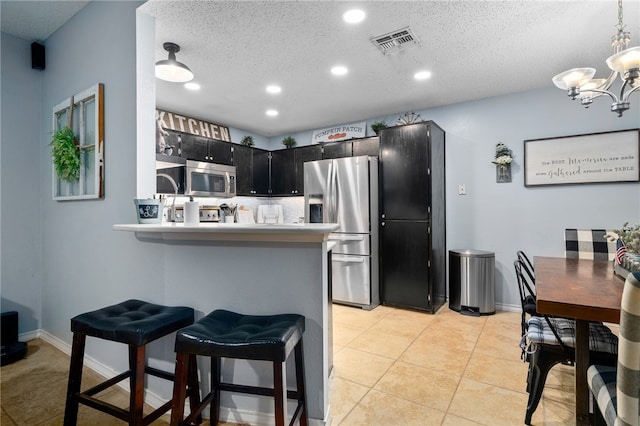 kitchen with a kitchen bar, kitchen peninsula, appliances with stainless steel finishes, and an inviting chandelier