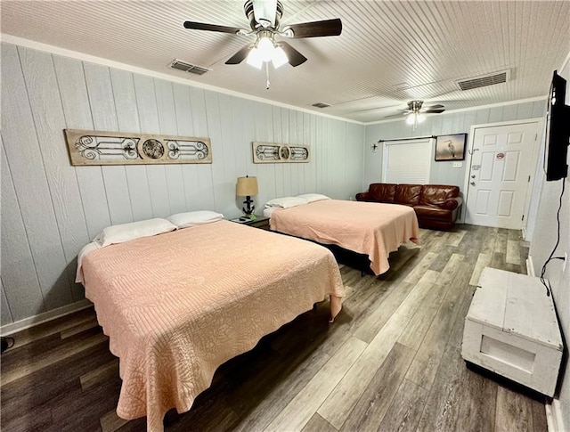 bedroom with ornamental molding, hardwood / wood-style floors, wooden walls, and ceiling fan