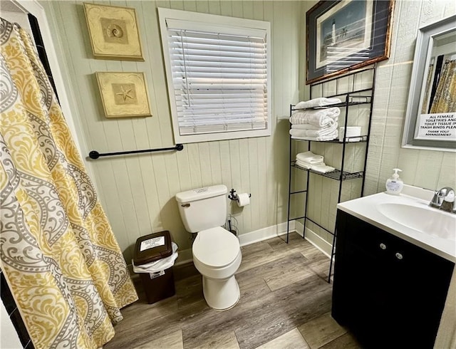 bathroom with hardwood / wood-style floors, wood walls, vanity, and toilet