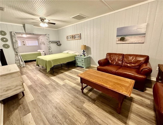 bedroom featuring ornamental molding, wood walls, light wood-type flooring, and ceiling fan