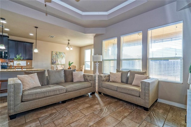 living room with a raised ceiling, ornamental molding, and a chandelier