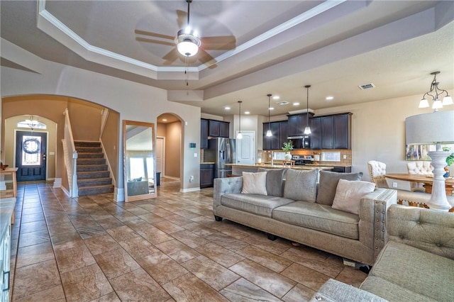 living room with ornamental molding, a raised ceiling, and ceiling fan with notable chandelier