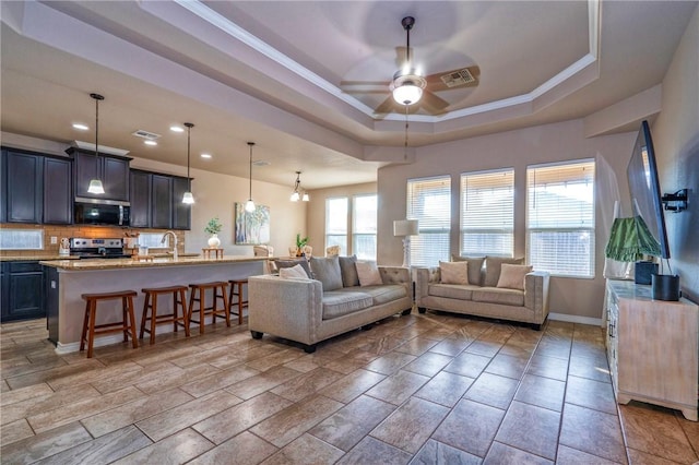 living room with sink, crown molding, ceiling fan with notable chandelier, and a raised ceiling