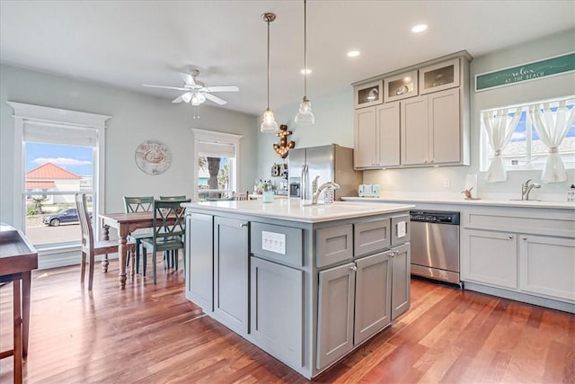 kitchen with appliances with stainless steel finishes, gray cabinetry, sink, hanging light fixtures, and an island with sink