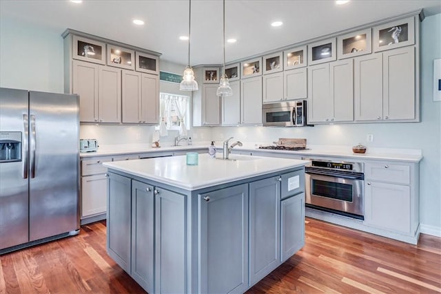 kitchen with sink, hardwood / wood-style floors, decorative light fixtures, a kitchen island with sink, and appliances with stainless steel finishes