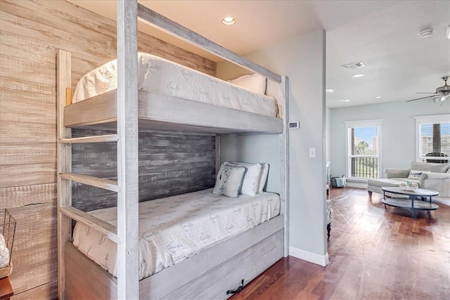 bedroom with ceiling fan, wooden walls, and dark wood-type flooring