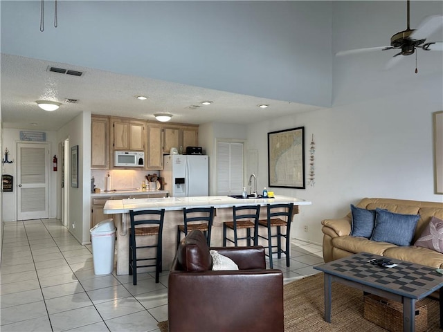 living room with light tile patterned flooring, ceiling fan, sink, and a textured ceiling