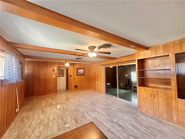 unfurnished living room with wooden walls, beamed ceiling, a ceiling fan, and wood finished floors