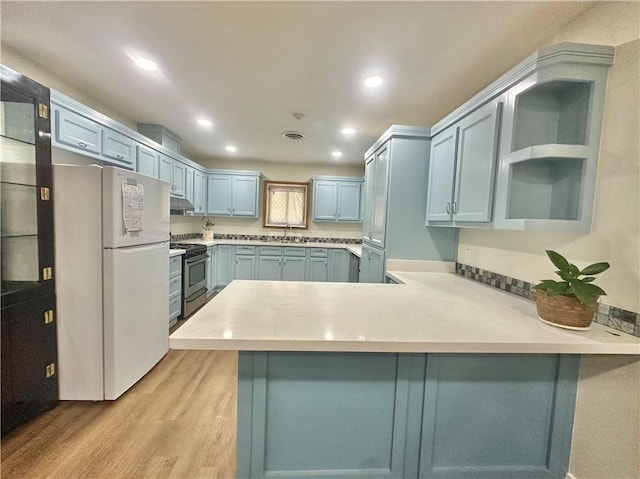 kitchen featuring freestanding refrigerator, a peninsula, open shelves, stainless steel range with gas cooktop, and light wood-type flooring