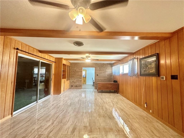 empty room featuring a ceiling fan, wooden walls, light wood-type flooring, and beam ceiling