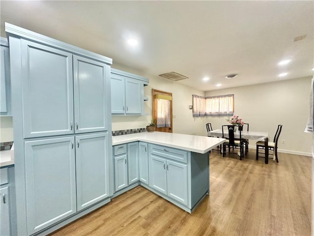 kitchen with a peninsula, blue cabinets, recessed lighting, light wood-style flooring, and light countertops