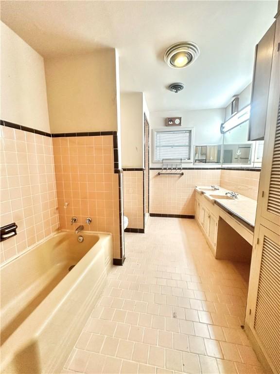 full bath with tile walls, toilet, vanity, tile patterned floors, and a garden tub