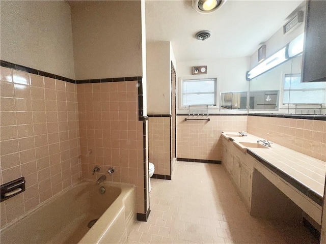 bathroom with tile walls, toilet, a bathtub, tile patterned flooring, and wainscoting