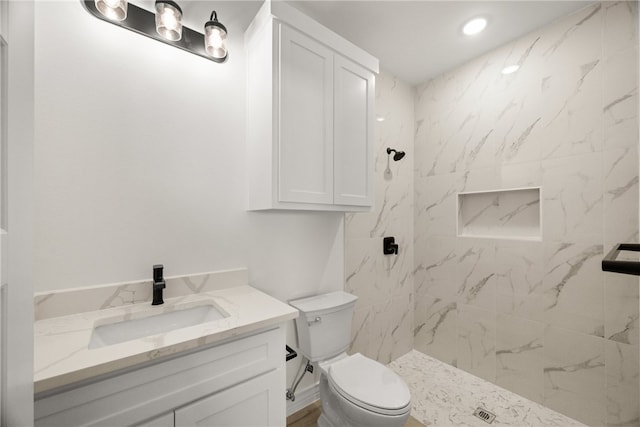 bathroom with a tile shower, vanity, and toilet