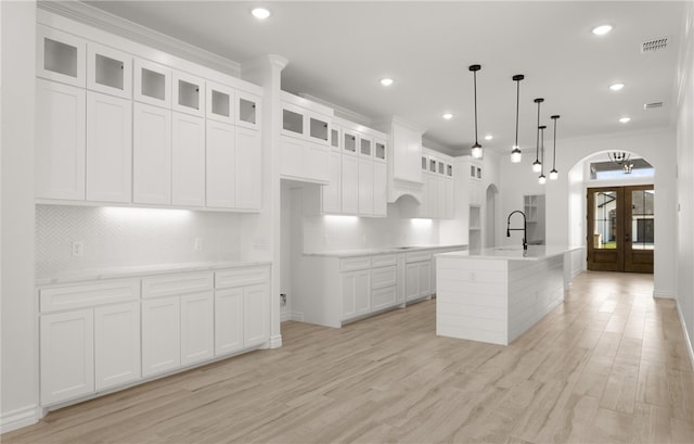 kitchen with a center island with sink, pendant lighting, white cabinets, and ornamental molding