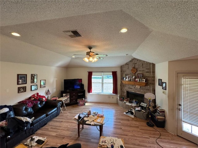 living room with vaulted ceiling, wood-type flooring, ceiling fan, a brick fireplace, and a textured ceiling