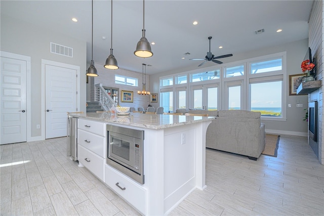 kitchen with white cabinetry, stainless steel microwave, a kitchen island, and decorative light fixtures