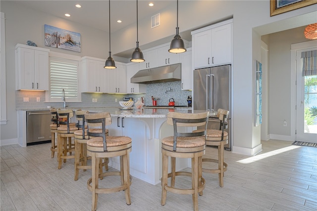 kitchen featuring light stone countertops, appliances with stainless steel finishes, pendant lighting, white cabinets, and a center island