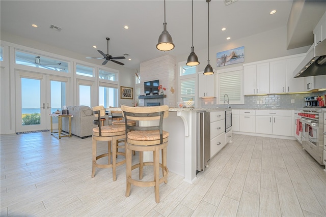 kitchen featuring decorative backsplash, light stone counters, high end stove, pendant lighting, and white cabinets