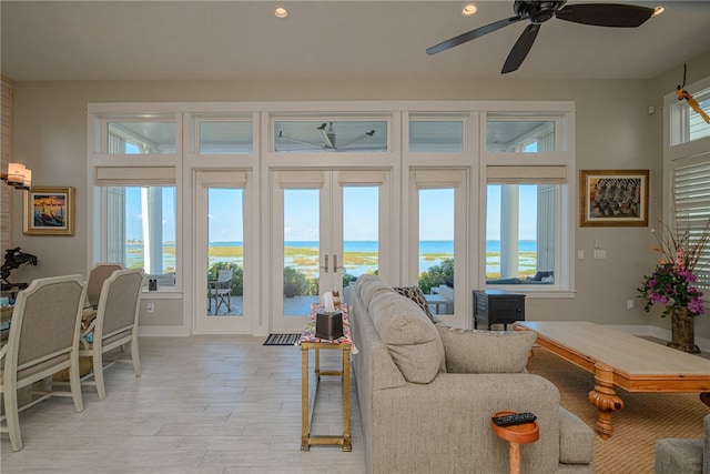 living room featuring french doors, light wood-type flooring, a water view, and ceiling fan