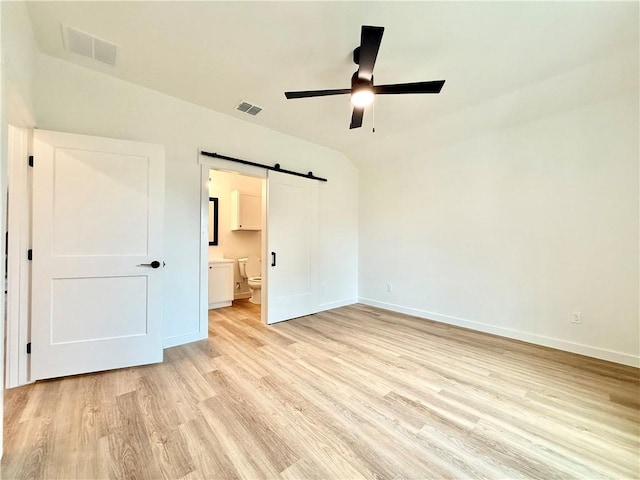 unfurnished bedroom with ensuite bathroom, ceiling fan, a barn door, light hardwood / wood-style flooring, and lofted ceiling