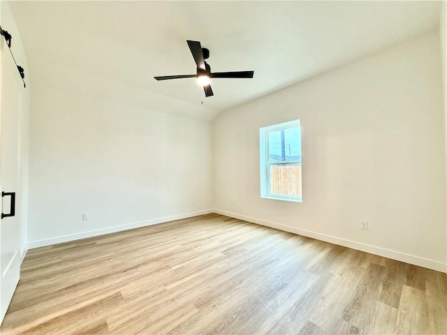 unfurnished room featuring ceiling fan, a barn door, and light hardwood / wood-style flooring