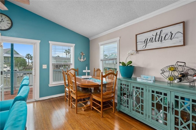dining space with ornamental molding, wood finished floors, lofted ceiling, baseboards, and a textured ceiling