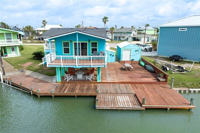 rear view of house with a deck with water view, a lawn, a residential view, an outdoor structure, and a shed