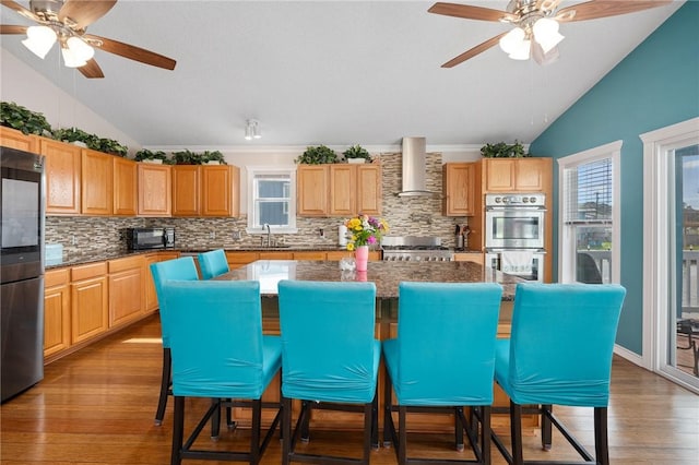 kitchen featuring a sink, appliances with stainless steel finishes, vaulted ceiling, and wall chimney range hood