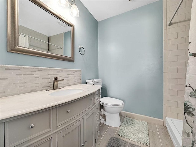 bathroom featuring tasteful backsplash, vanity, baseboards, toilet, and tiled shower