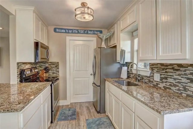 kitchen featuring stainless steel appliances, light wood-style floors, white cabinetry, a sink, and light stone countertops