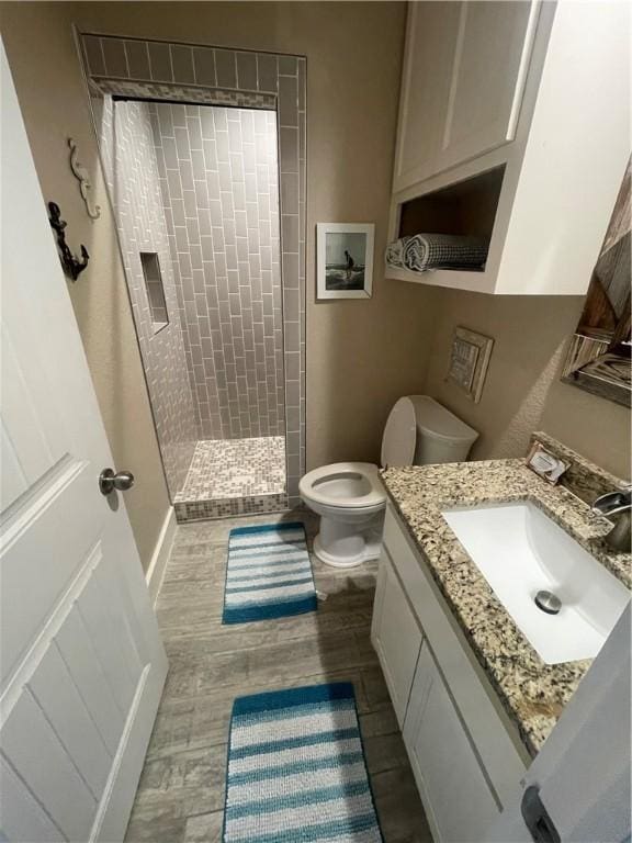 full bath featuring toilet, a tile shower, wood finished floors, and vanity