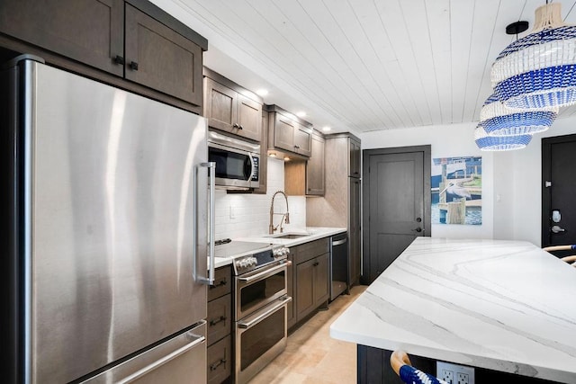 kitchen featuring pendant lighting, appliances with stainless steel finishes, tasteful backsplash, a sink, and light stone counters