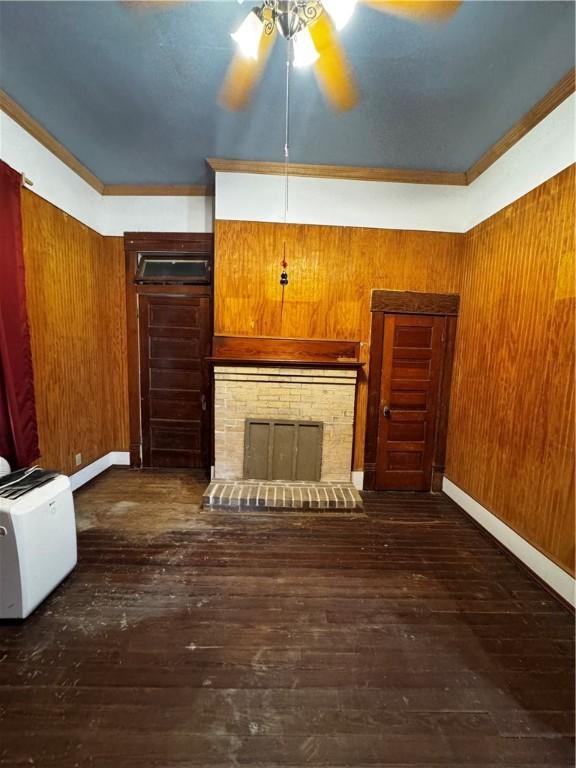 unfurnished living room with wood walls, a fireplace, dark hardwood / wood-style floors, and ornamental molding