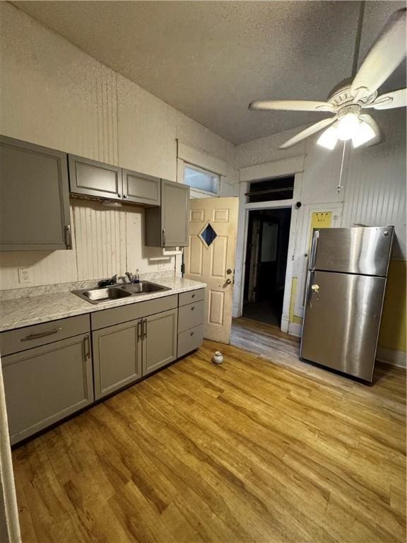 kitchen with stainless steel refrigerator, ceiling fan, sink, light hardwood / wood-style floors, and gray cabinets