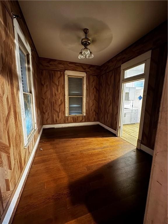 empty room with dark hardwood / wood-style floors, ceiling fan, a wealth of natural light, and wooden walls