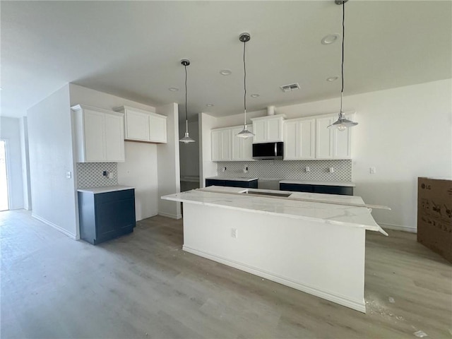 kitchen with white cabinetry, decorative light fixtures, light stone countertops, and a kitchen island