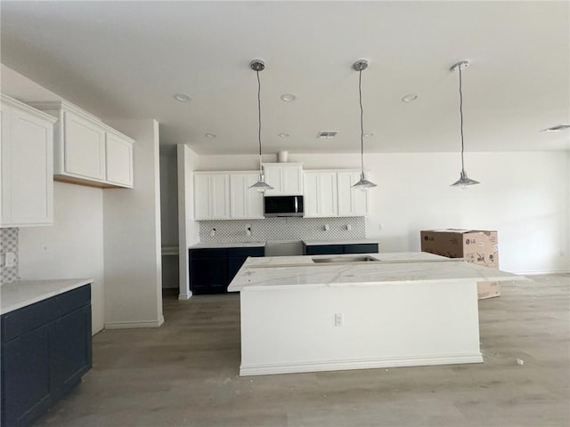 kitchen with white cabinetry, hardwood / wood-style floors, decorative backsplash, a kitchen island, and decorative light fixtures