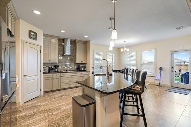 kitchen featuring pendant lighting, a kitchen island with sink, sink, wall chimney exhaust hood, and a chandelier