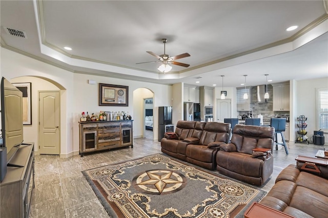 living room with bar area, ceiling fan, crown molding, and a tray ceiling