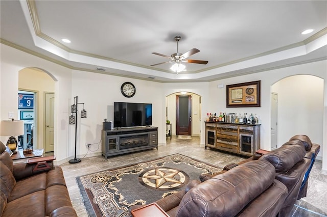 living room featuring bar, a raised ceiling, ceiling fan, and crown molding