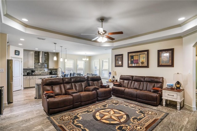 living room with ceiling fan with notable chandelier, a raised ceiling, and ornamental molding