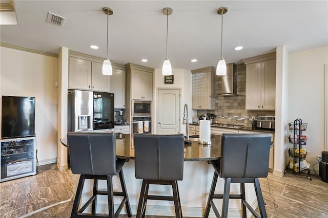 kitchen with a center island with sink, wall chimney range hood, decorative backsplash, dark stone countertops, and stainless steel appliances