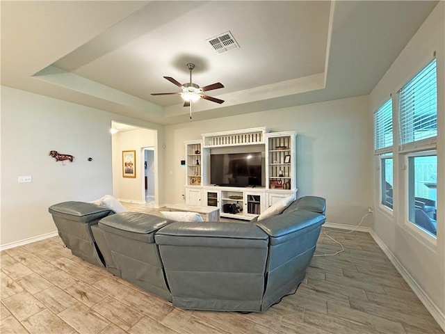 living area with a raised ceiling, ceiling fan, wood finished floors, and baseboards