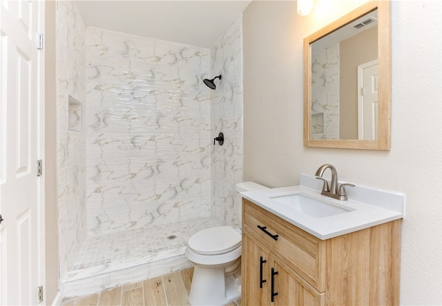 bathroom with tiled shower, hardwood / wood-style floors, vanity, and toilet