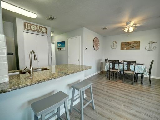 kitchen with a kitchen bar, stone countertops, hardwood / wood-style flooring, kitchen peninsula, and ceiling fan