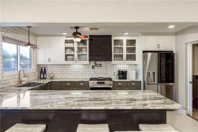 kitchen featuring light stone counters, appliances with stainless steel finishes, a sink, and glass insert cabinets