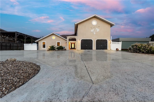 view of front of house featuring a garage, stucco siding, driveway, and fence