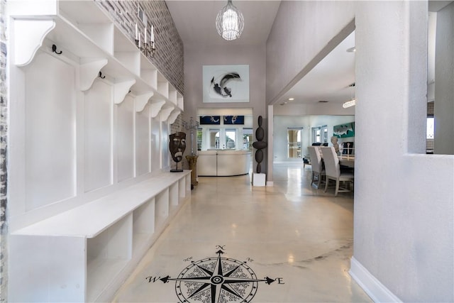 mudroom featuring a towering ceiling, concrete floors, baseboards, and a notable chandelier